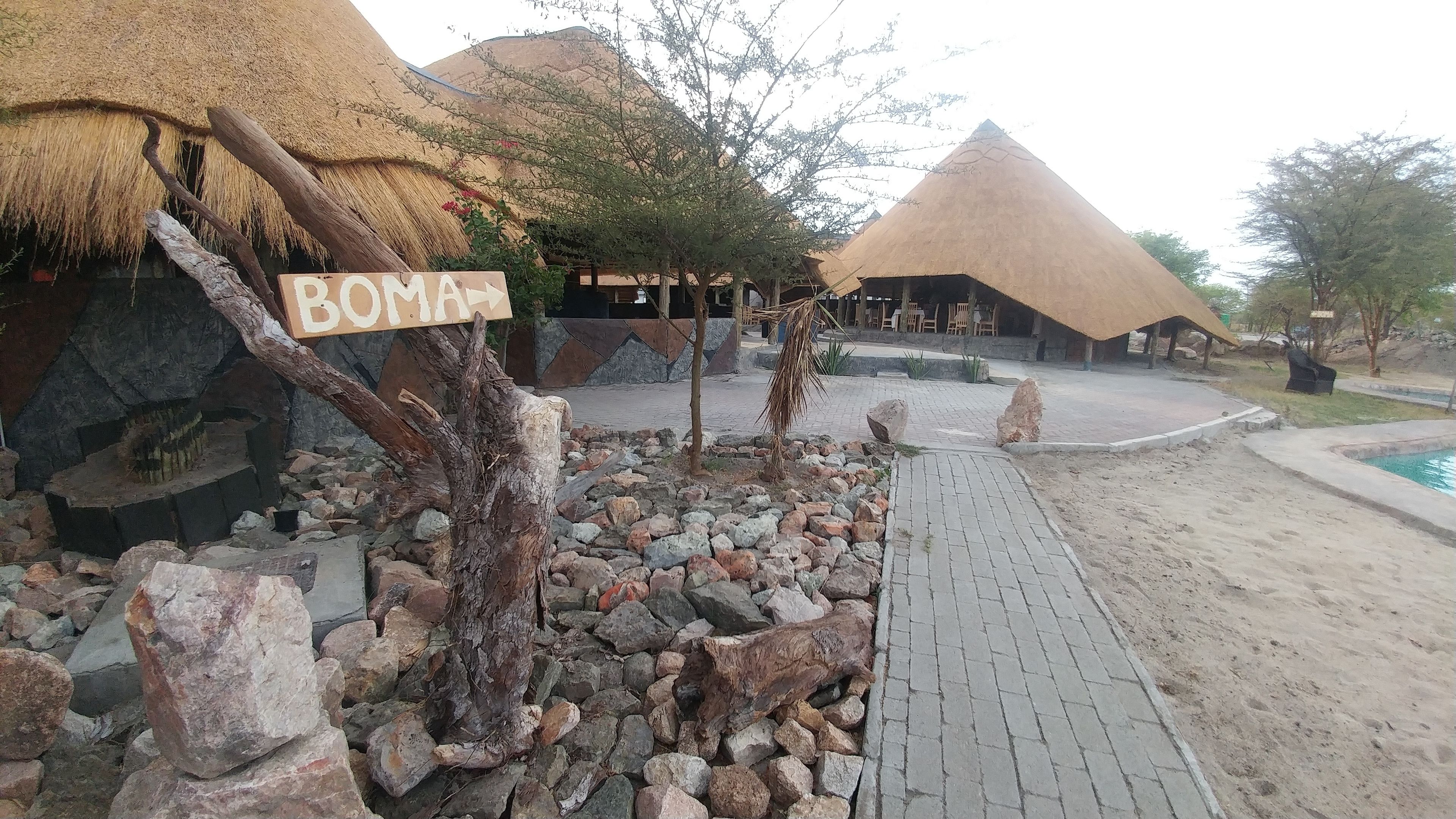 A thatched-roof structure labeled 'BOMA' with a paved walkway leading to a pool area.
