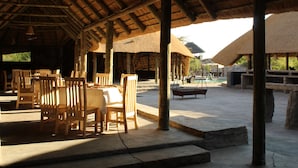 Un espace de restauration en plein air avec des tables et des chaises en bois, des structures à toits de chaume et un sol pavé de pierres.