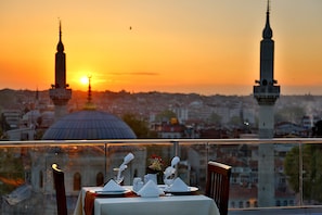 A table set for two with a view of a cityscape at sunset, including two prominent towers and a dome.