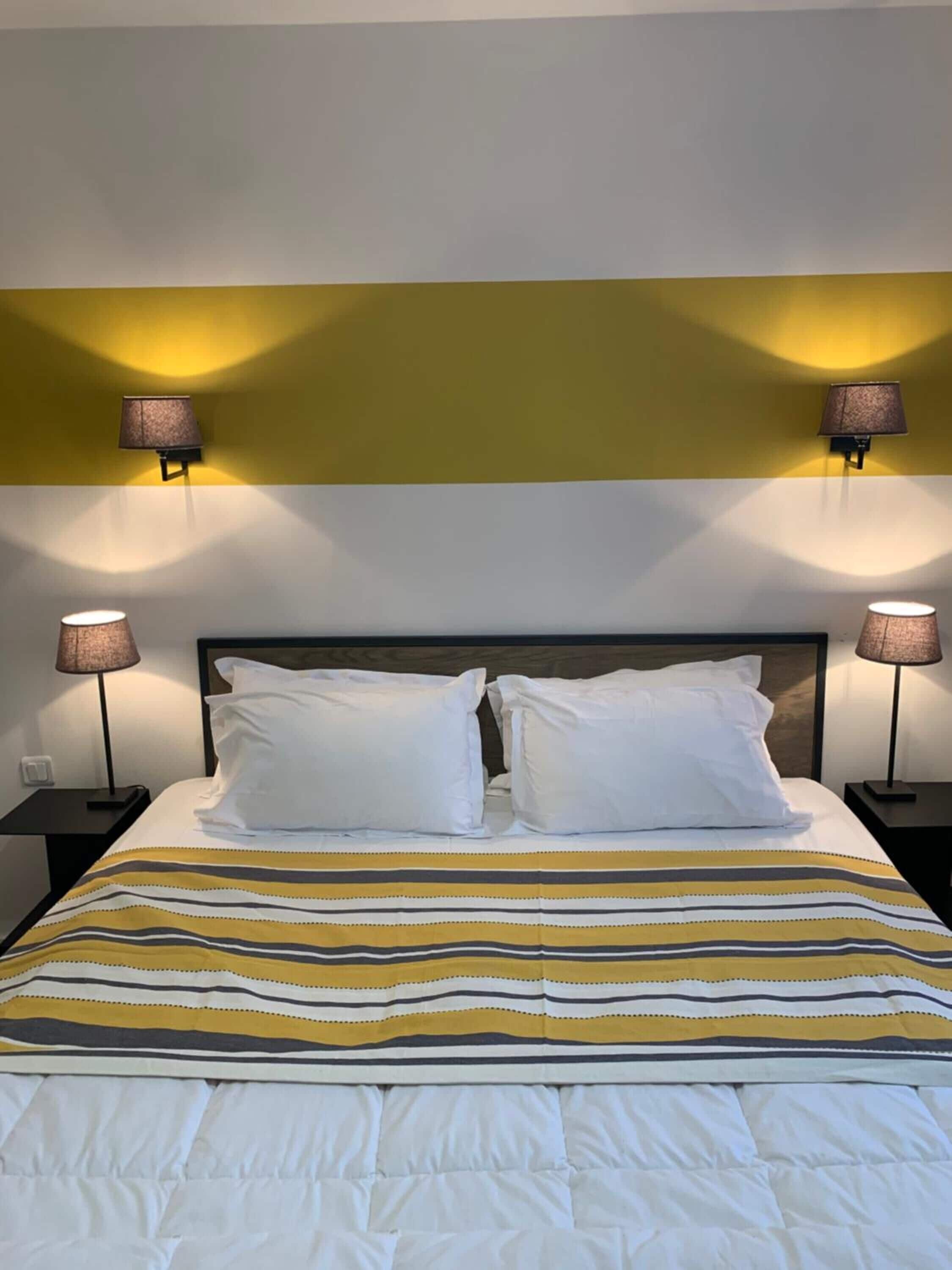 Une chambre d’hôtel avec un lit, deux tables de chevet, deux lampes fixées au mur et une couvre-lit à rayures.