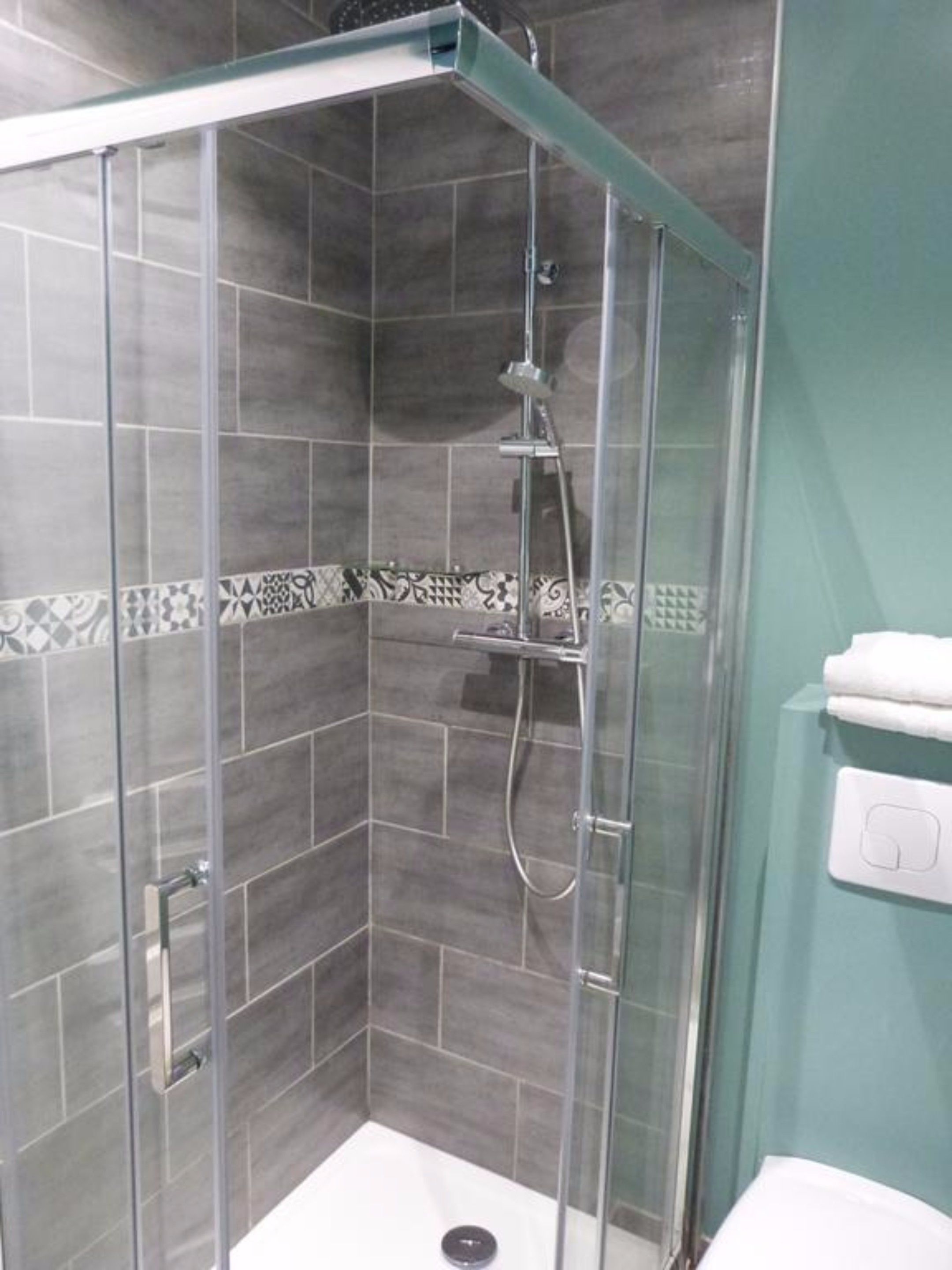Una cabina de ducha con paredes de vidrio, piso de azulejos y un rociador.