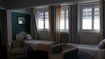 A hotel room with two single beds, a chair, and a window with curtains.