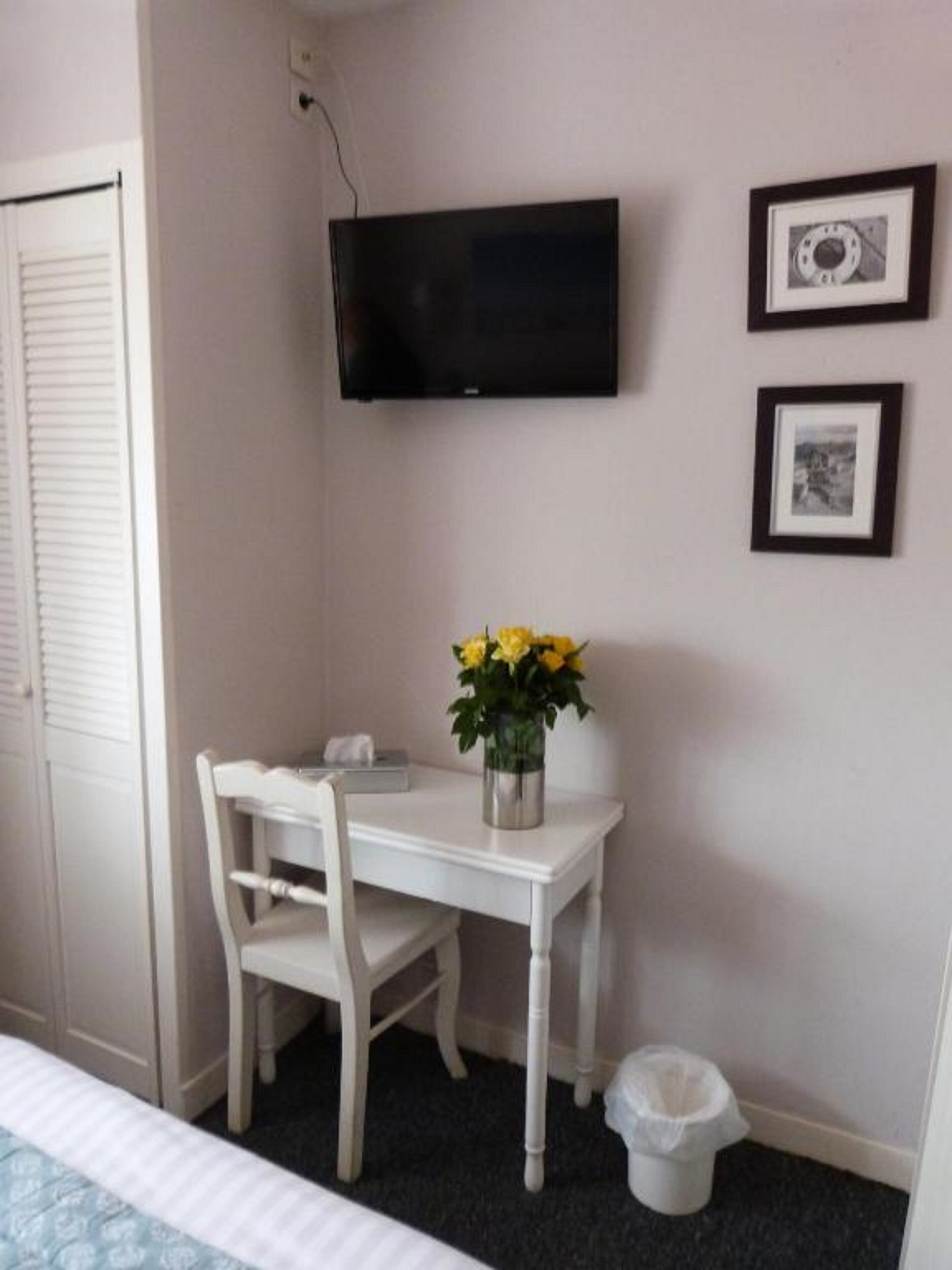 Una habitación pequeña con un escritorio blanco, una silla, un televisor instalado en la pared y un cubo de basura.