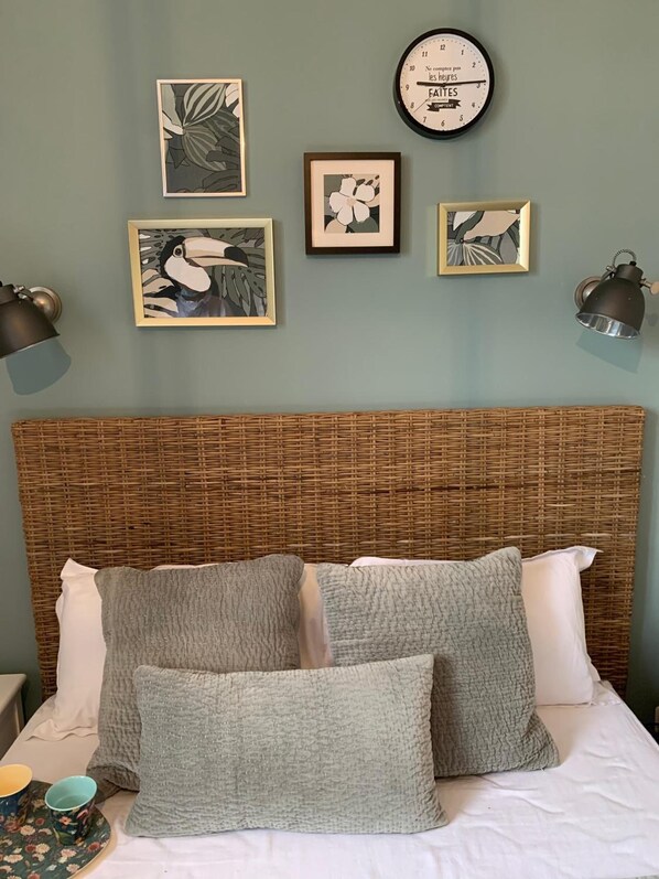 A bed with a woven headboard, grey and white pillows, and a framed picture of a bird.