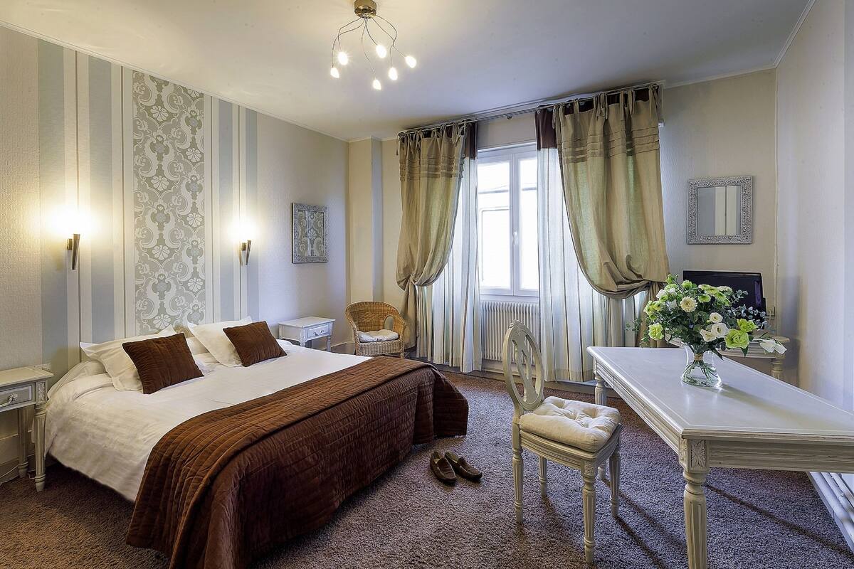 A hotel room with a large bed, a desk, a chair, and a window with curtains.