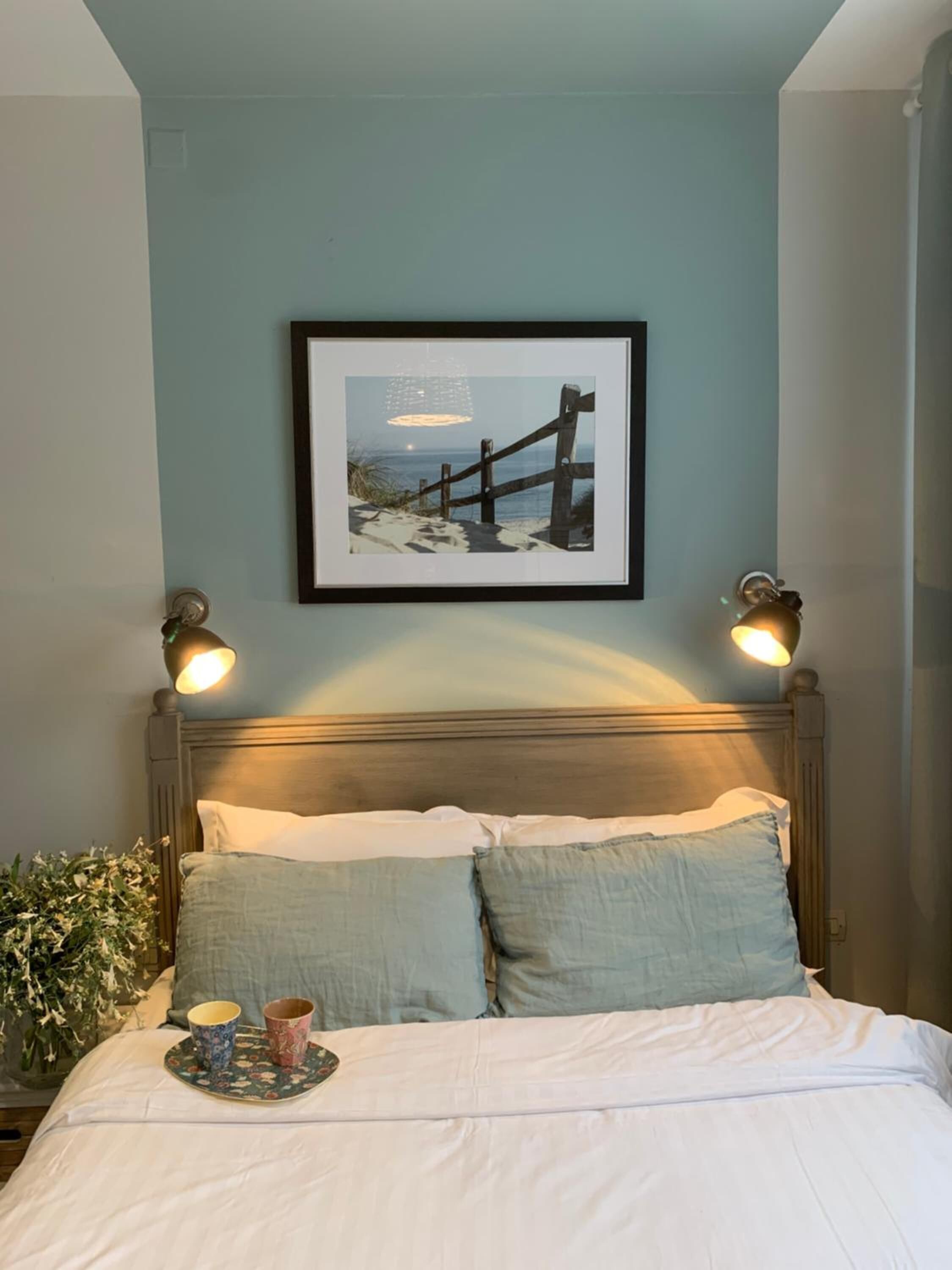 A neatly made bed with two pillows, a framed picture on the wall, and two bedside lamps.