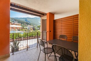 A balcony with a table and chairs, a view of a mountainous landscape, and a pool area. - Residence Maroadi (Nago-Torbole)