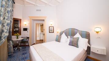 Quarto de hotel com uma cama grande, uma mesa com cadeira e uma pequena mesa com um vaso de flores.