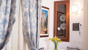 A room with a white round table, a vase with yellow flowers, a framed picture, a wooden door with glass panels, and a wall-mounted light fixture. - B&B Maiurè (Maiori)
