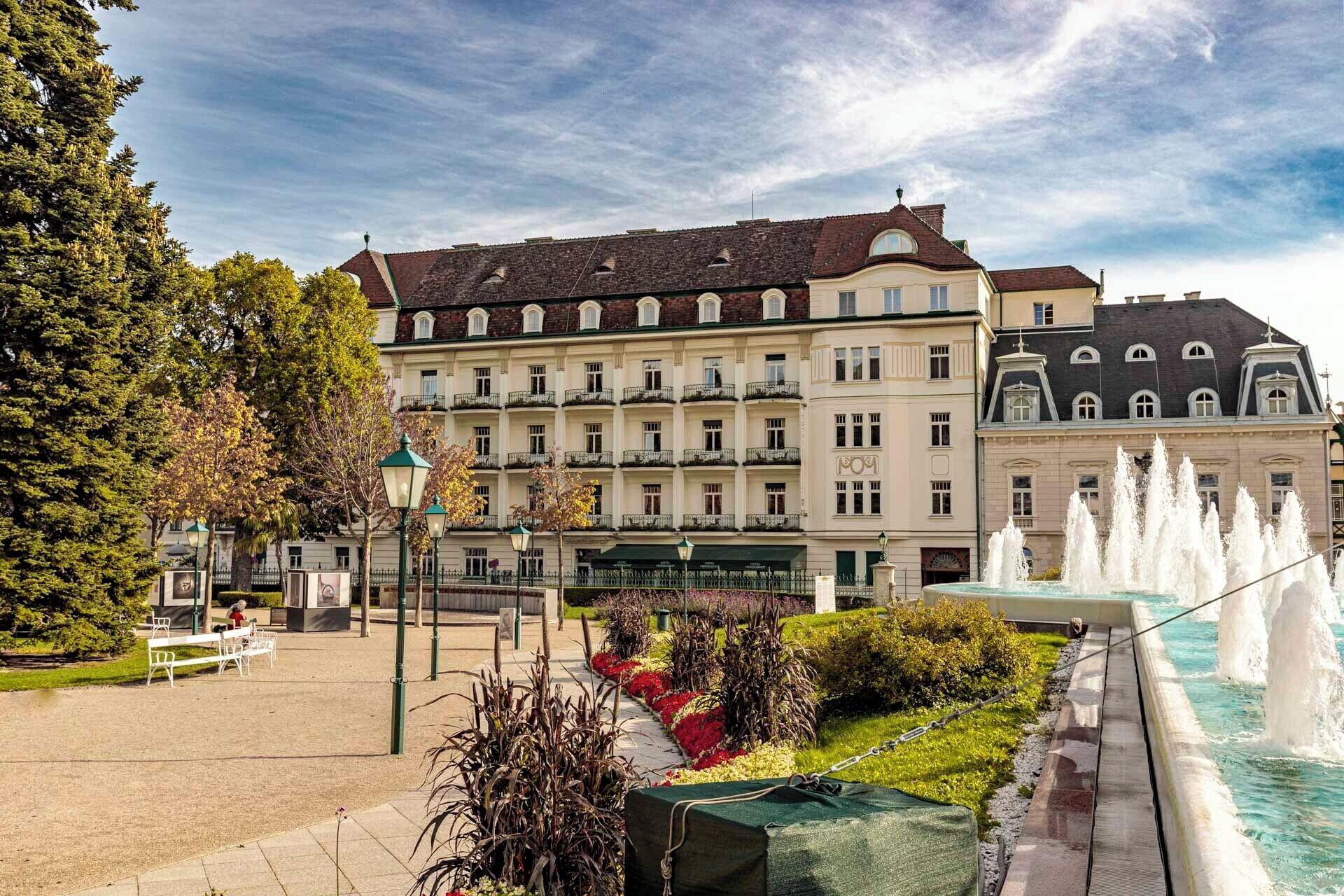 A historic building with multiple balconies, a fountain, and a garden with benches.
