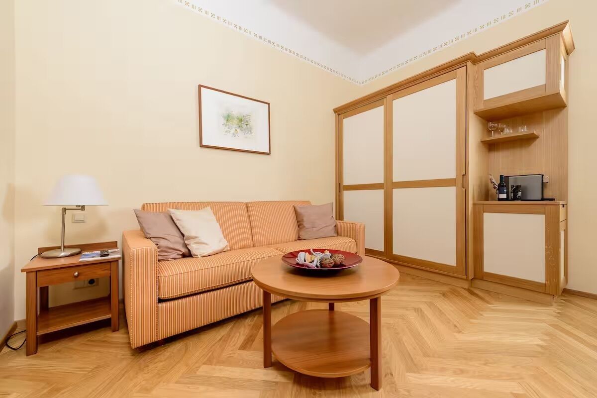 Ein Zimmer mit einem gestreiften Sofa, einem kleinen Tisch mit einer Schale, einem Nachttisch, einer Lampe und einem Holzschrank.