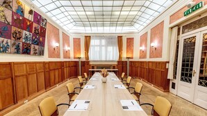 Un salón de conferencias con una larga mesa, sillas, un centro de mesa floral y un mural en la pared.