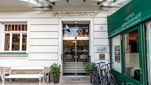Entrada de un hotel con un letrero que dice 'HOTEL HERZOGHOF', un banco, plantas en macetas y bicicletas estacionadas afuera.