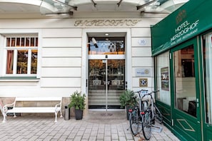 A hotel entrance with a sign reading 'HOTEL HERZOGHOF,' a bench, potted plants, and bicycles parked outside.