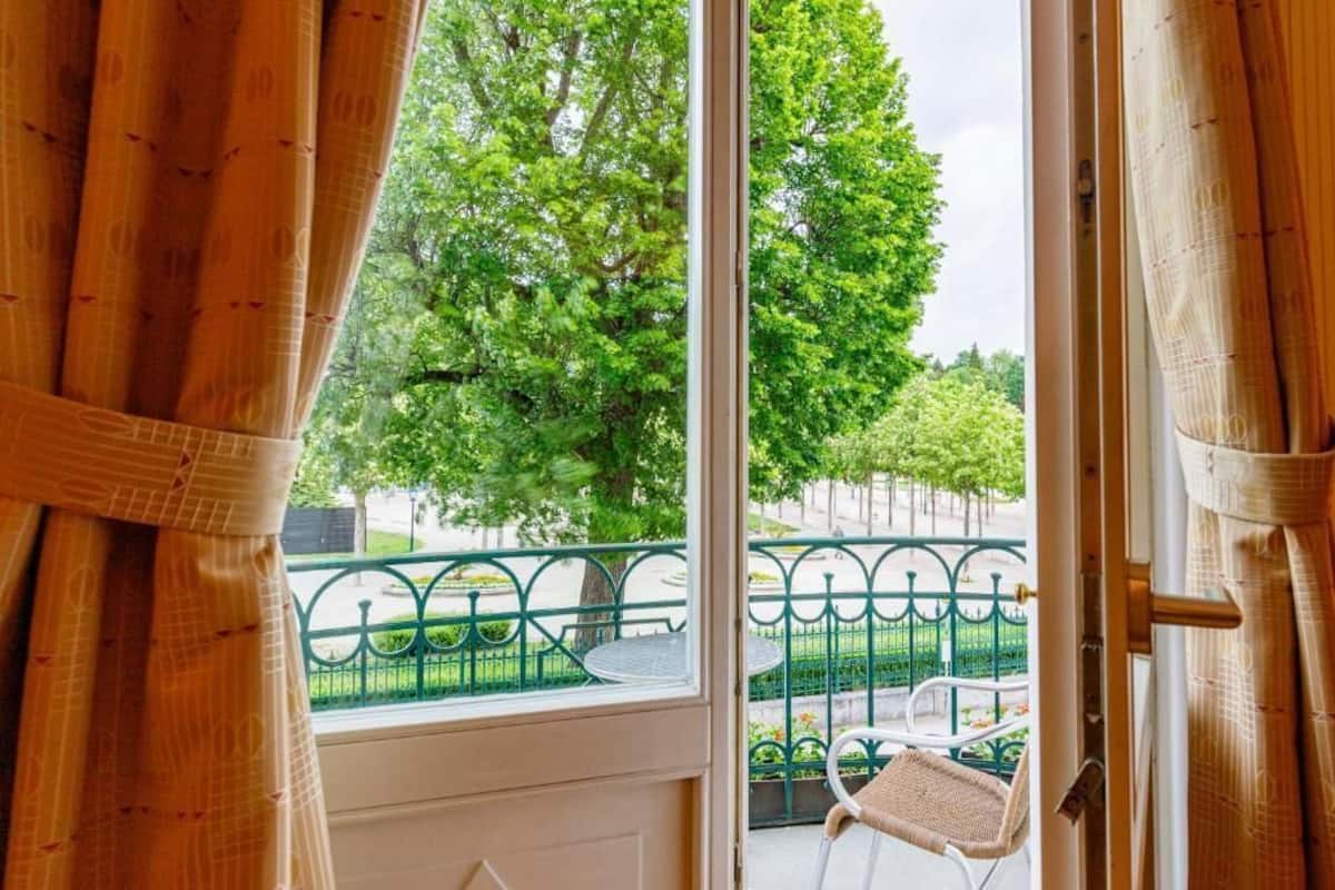 A balcony with a view of a green park and a metal railing.