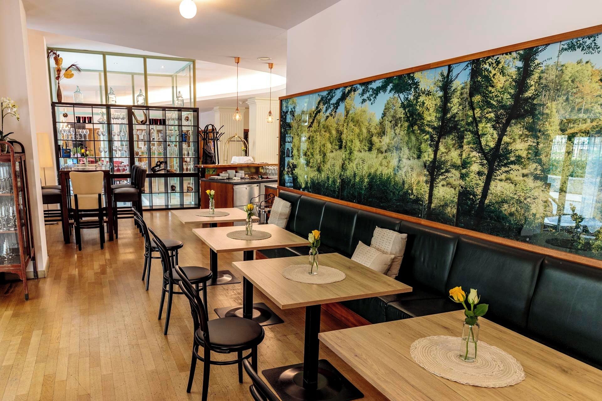 Un restaurant avec des tables en bois, des chaises noires, une vitrine et une grande fresque représentant une forêt.