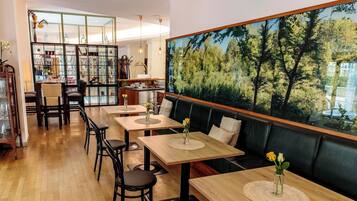 Un restaurant avec des tables en bois, des chaises noires, une vitrine et une grande fresque représentant une forêt.