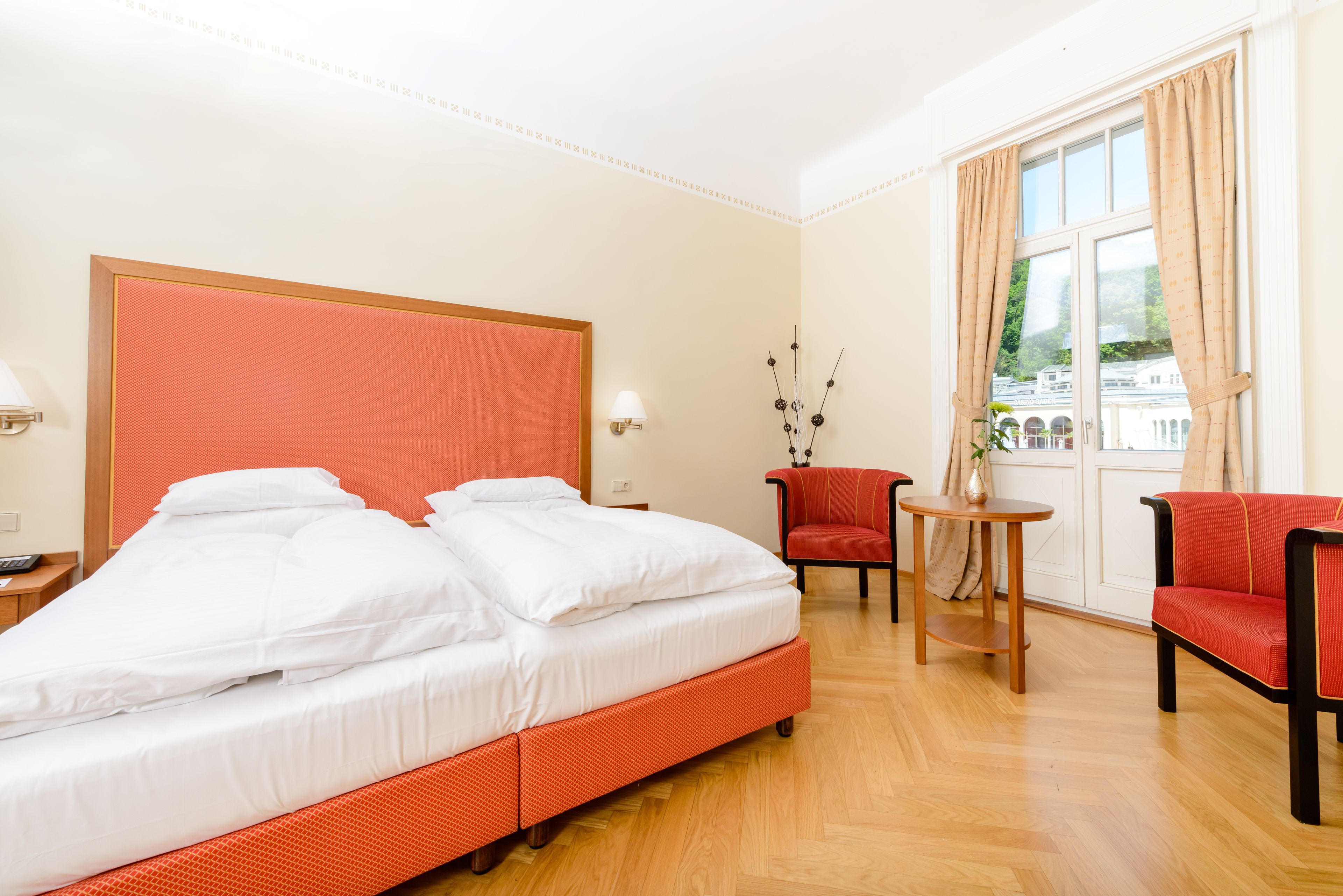 Una camera d'albergo con un letto grande, due sedie, un tavolino e una finestra con tende.