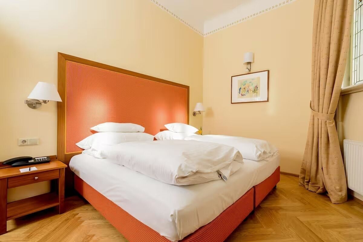 A hotel room with a bed, bedside table, lamp, and artwork on the wall.