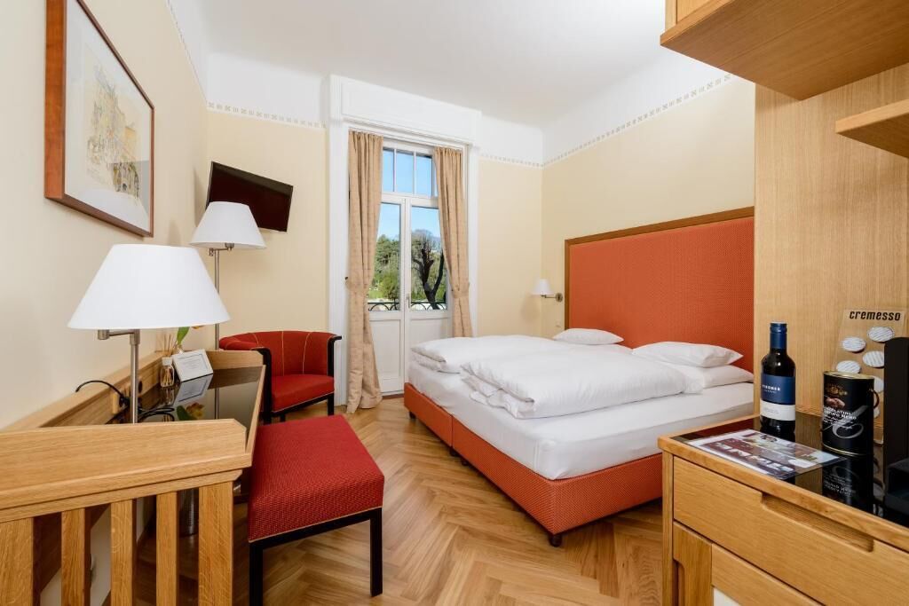 Een hotelkamer met een bed, een bureau, een stoel, een lamp en een raam met gordijnen.