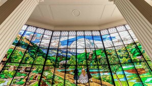 Un ventanal de vitrales con una escena de paisaje, columnas blancas y un techo con molduras decorativas.