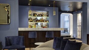 A modern bar area with a marble countertop and shelves of liquor bottles. There are two blue upholstered chairs and a grey sofa with dark cushions. - GKK Exclusive Private Suite (Rome)