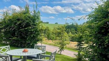 Eine Terrasse mit einem runden Tisch und Stühlen, umgeben von viel Grün und blauem Himmel.