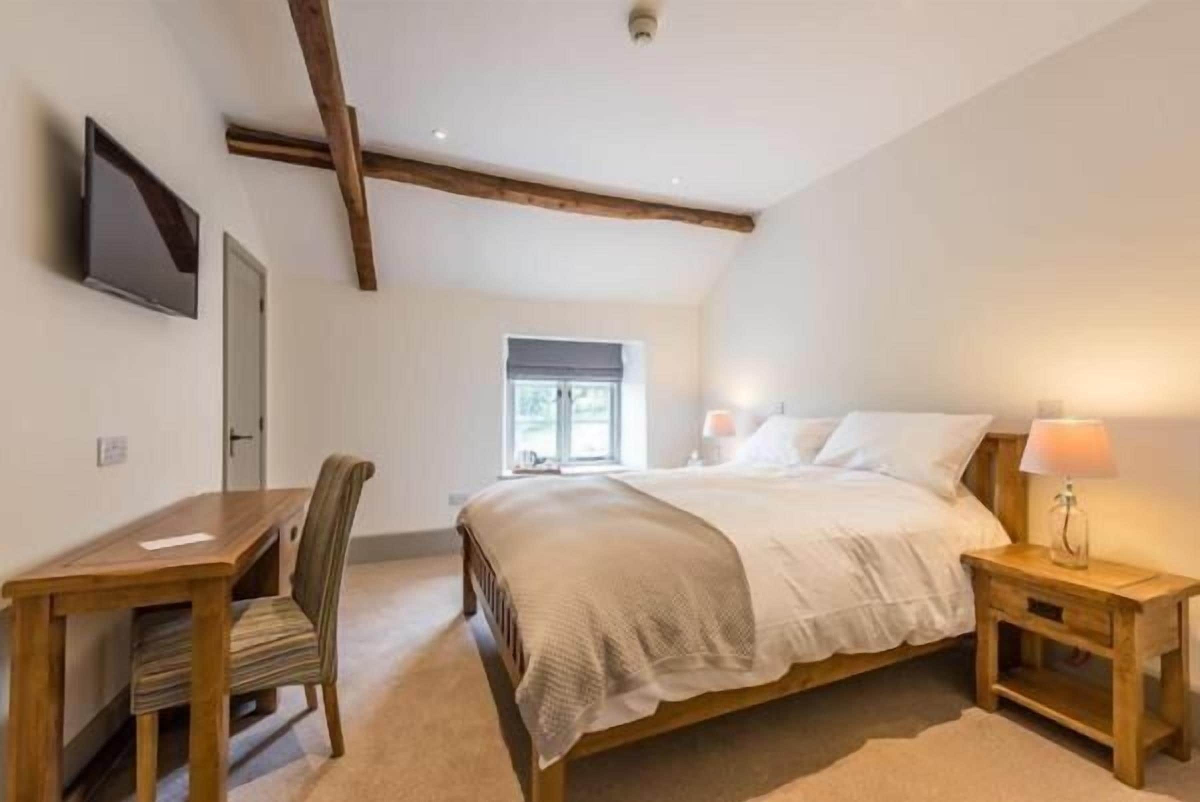 A bedroom with a bed, bedside tables, a desk, a chair, and a television on the wall.
