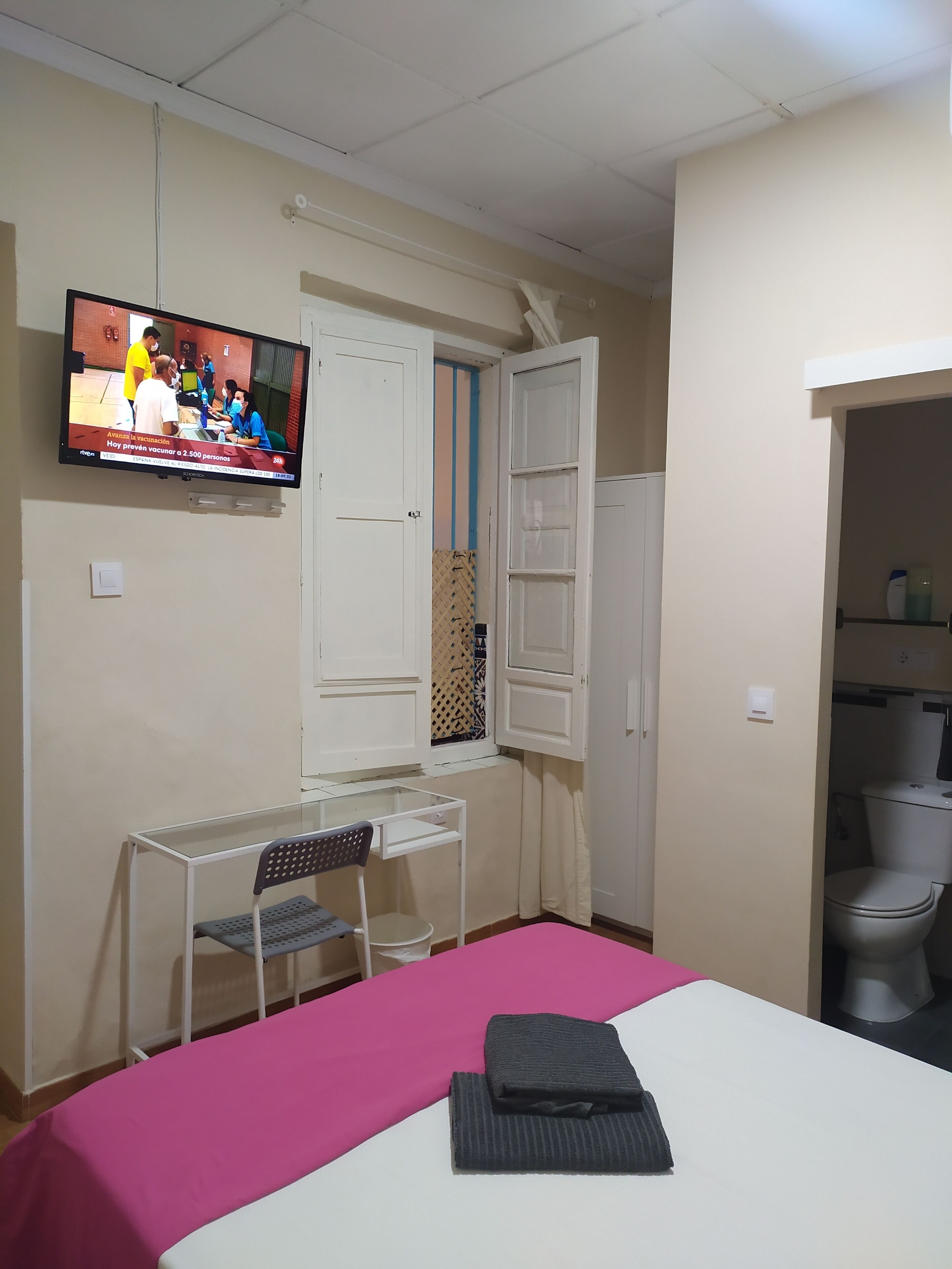 Una habitación con cama, escritorio, silla, televisor y baño.