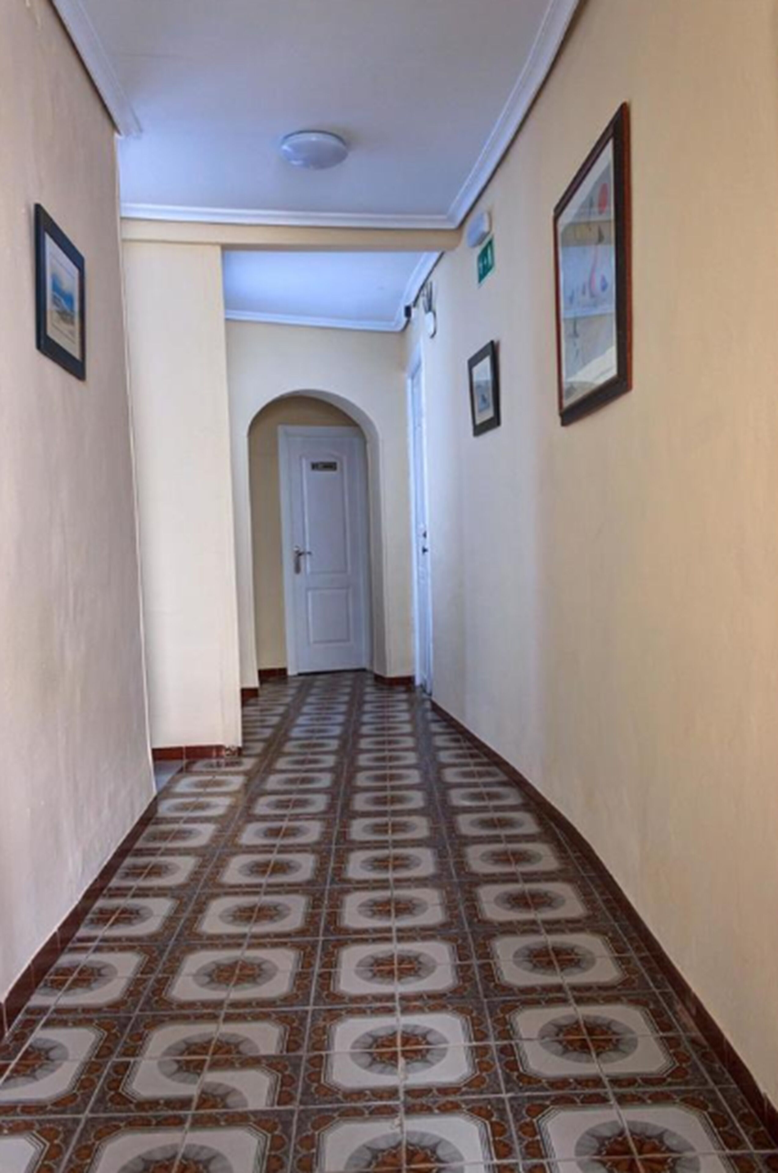 A hallway with patterned tile flooring, white walls, and framed pictures.