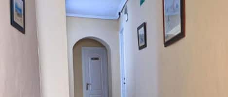 A hallway with patterned tile flooring, white walls, and framed pictures.