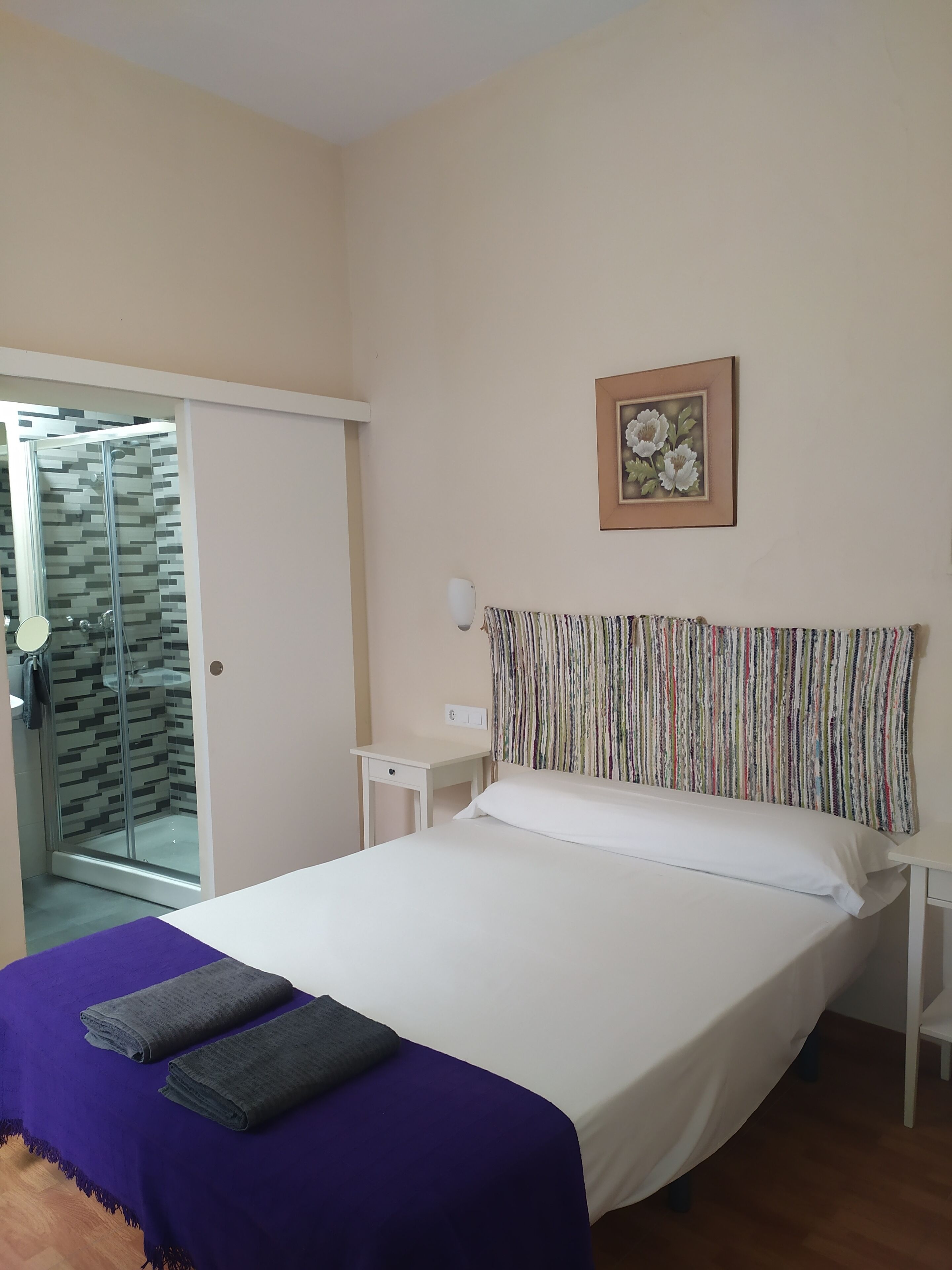 Ein Schlafzimmer mit Bett, Nachttisch, Duschbereich und einem Wandbild.