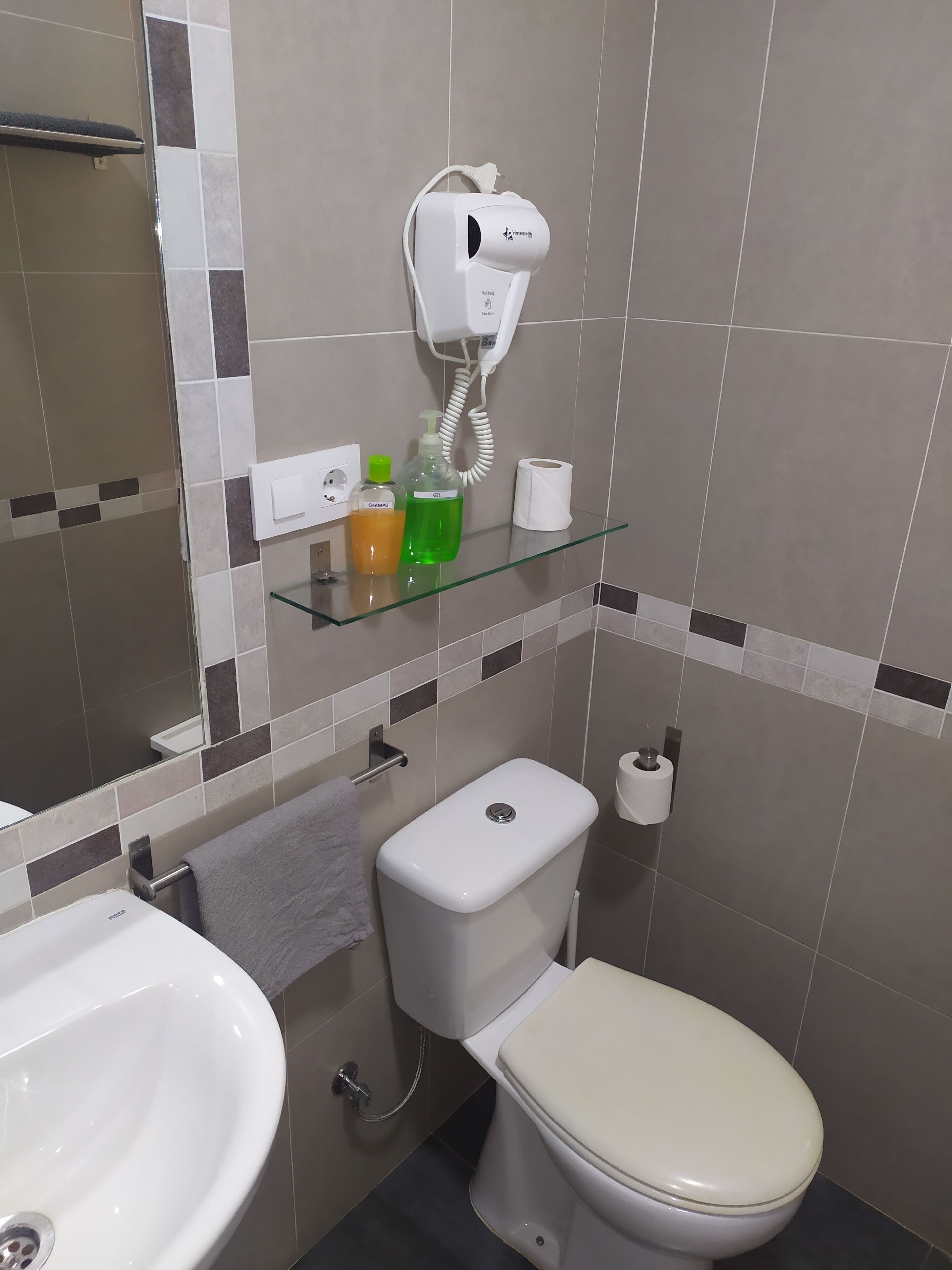 Un baño con inodoro, lavamanos y un secador de pelo montado en la pared.