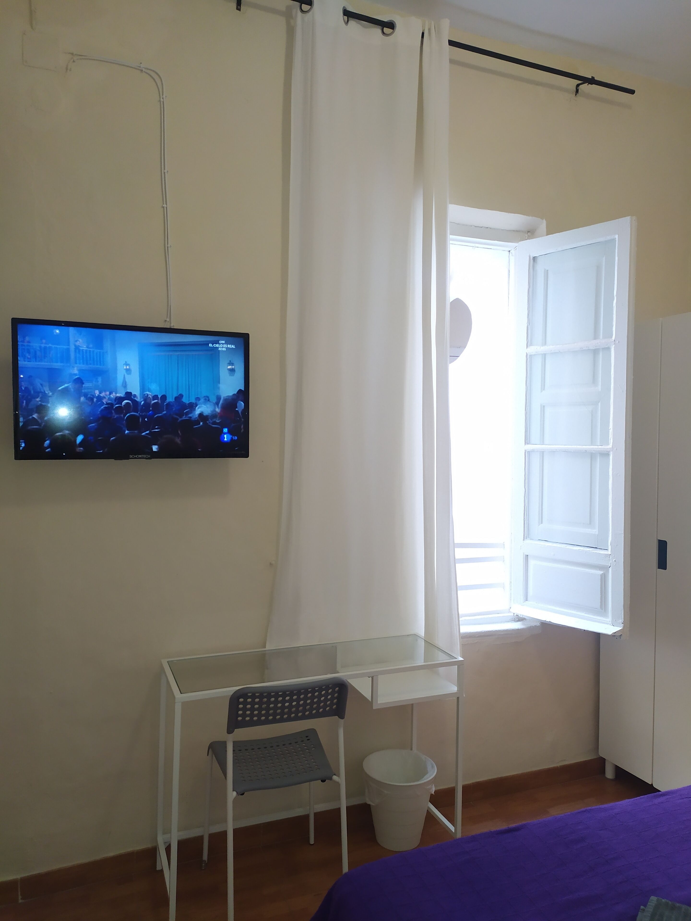 A room with a bed, a desk with a chair, a television, a window with curtains, and a wardrobe.