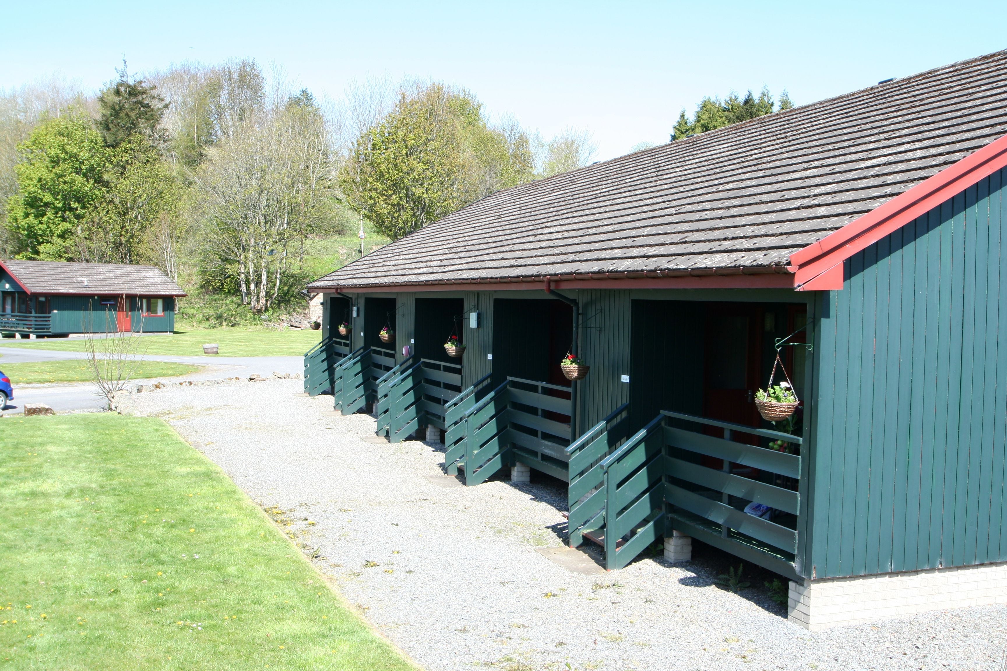 A row of green wooden buildings with sloped roofs, each with a porch and hanging baskets.
