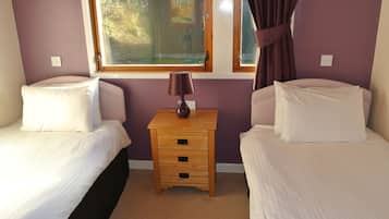A bedroom with two beds, a nightstand, and a window with curtains.
