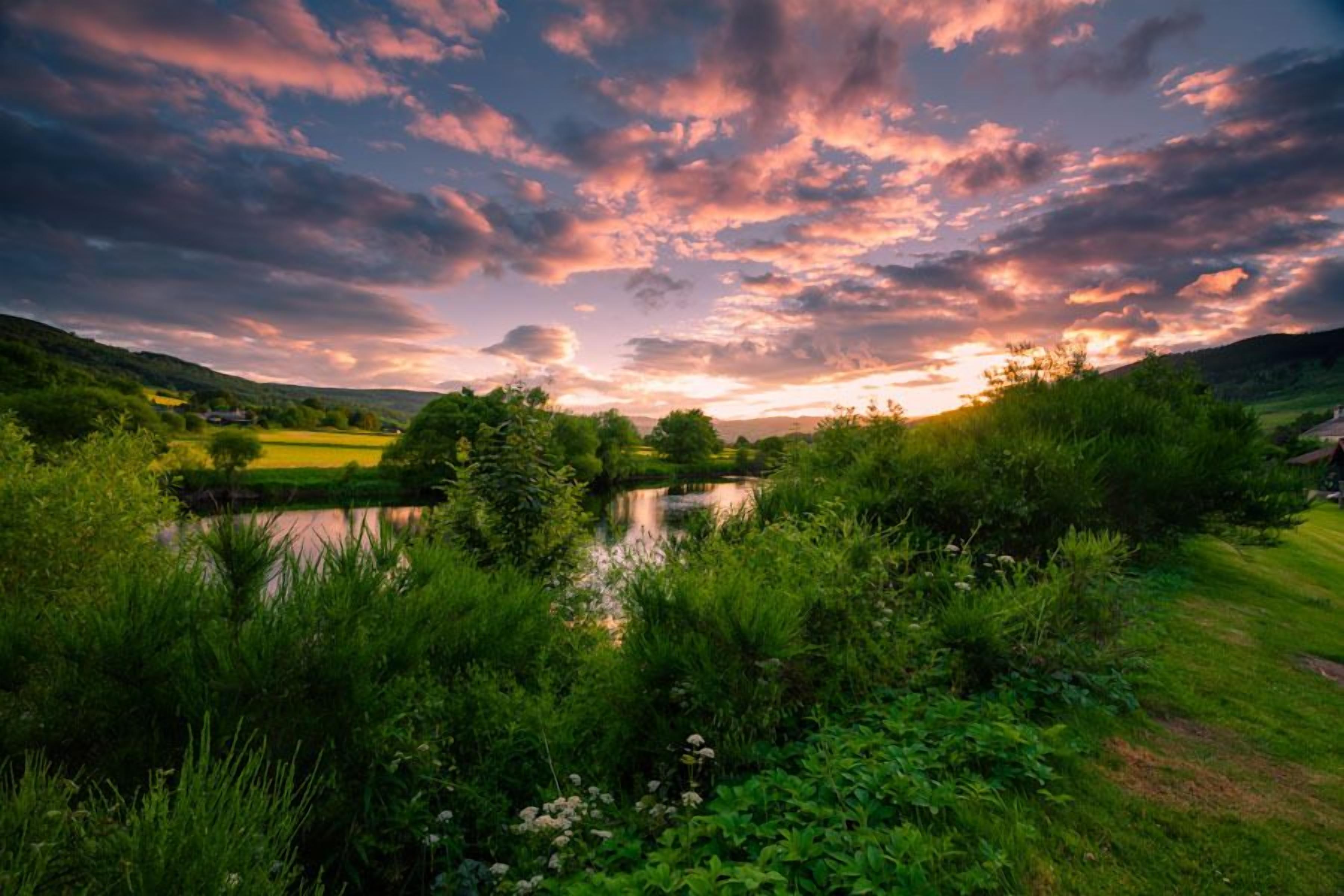 Un paysage naturel comprenant une étendue d’eau, une végétation luxuriante et un ciel au coucher du soleil.