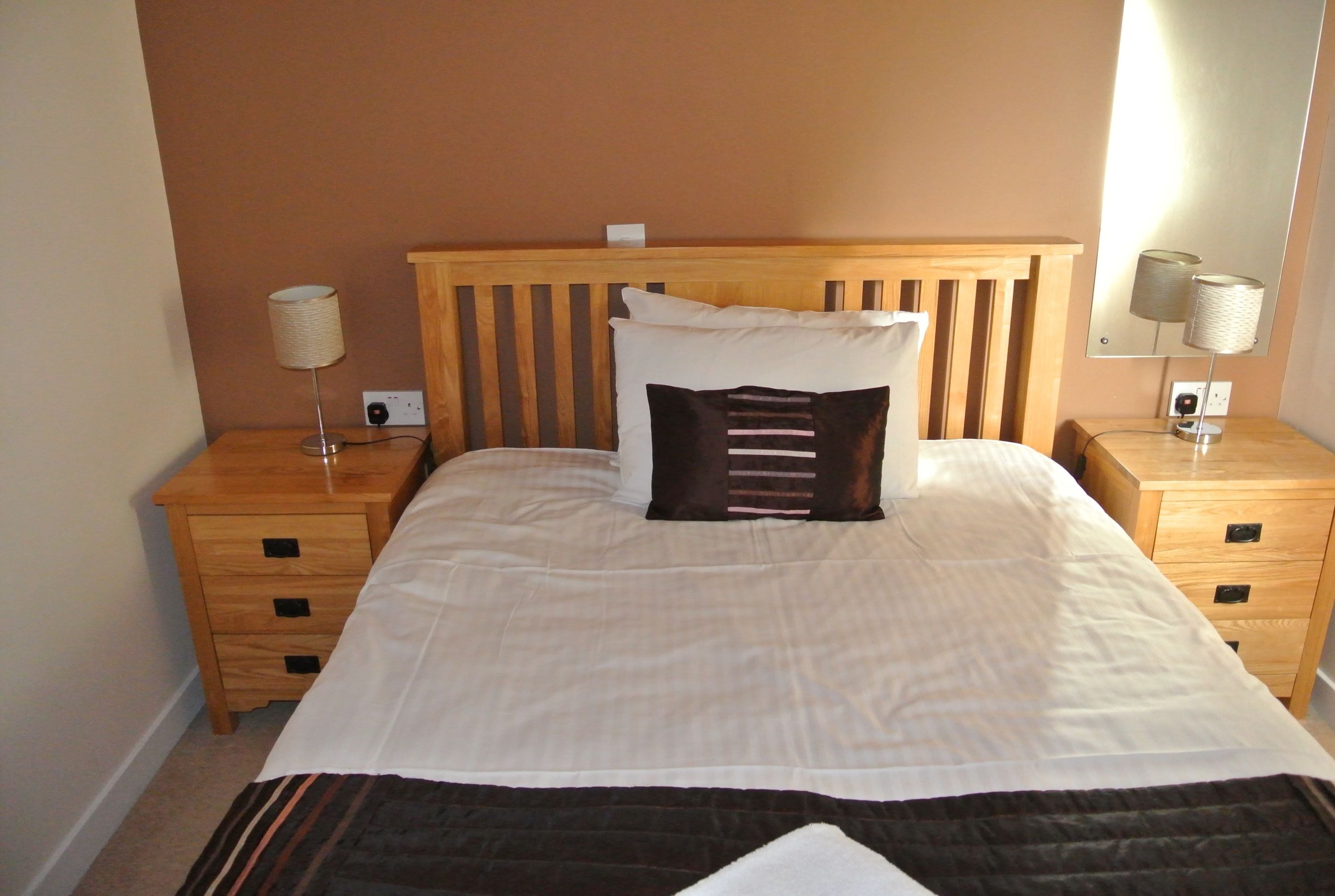 A neatly made bed with a wooden headboard, two bedside tables with lamps, and a wall-mounted mirror.