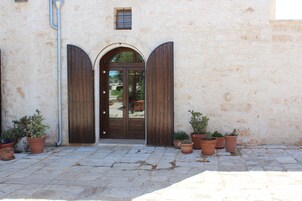 Un edificio de fachada de piedra, puerta de madera con arco y varios maceteros con plantas en la entrada.