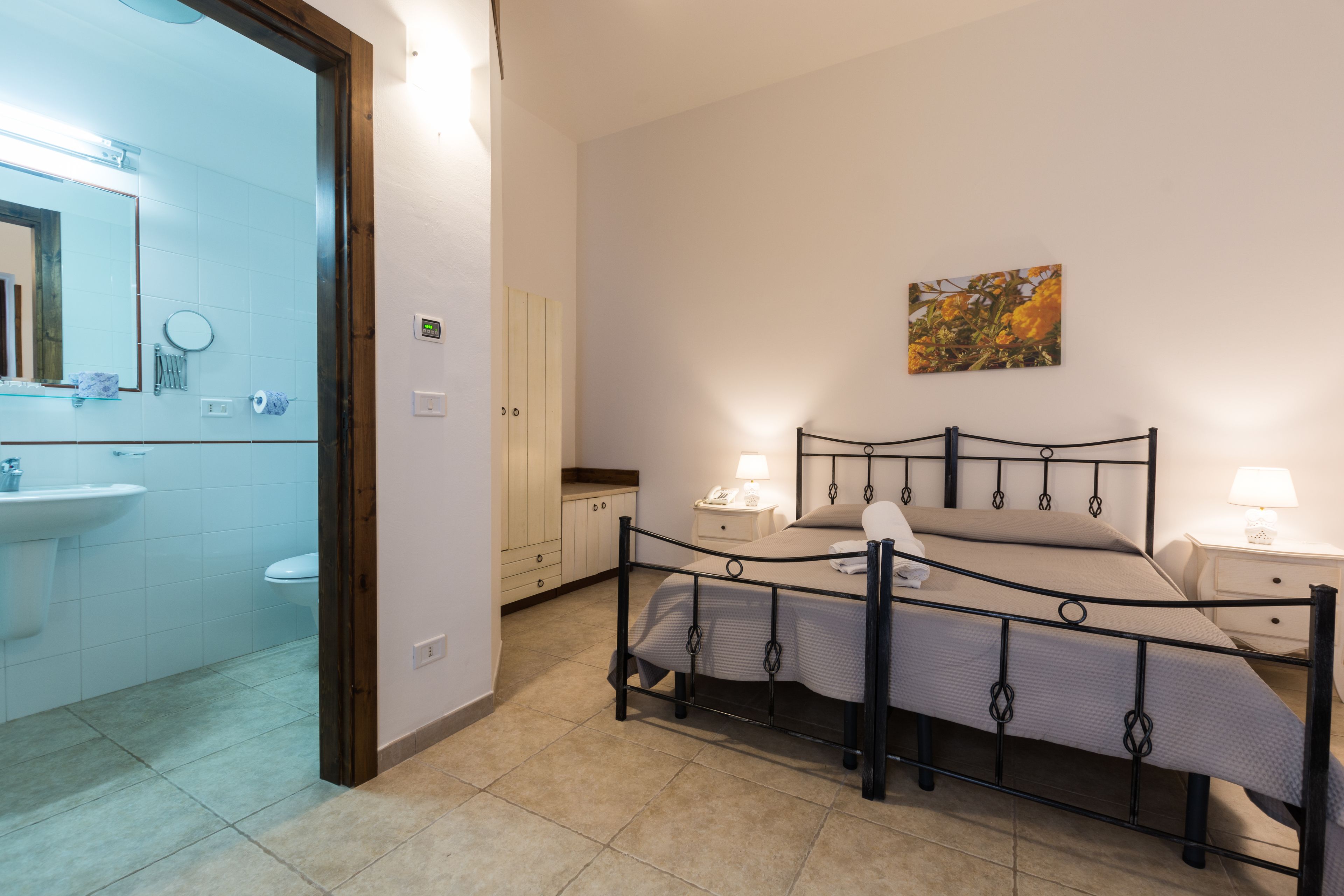 Une chambre à coucher comprenant un lit, des tables de chevet, une commode, un miroir et une salle de bain visible à travers une porte ouverte.