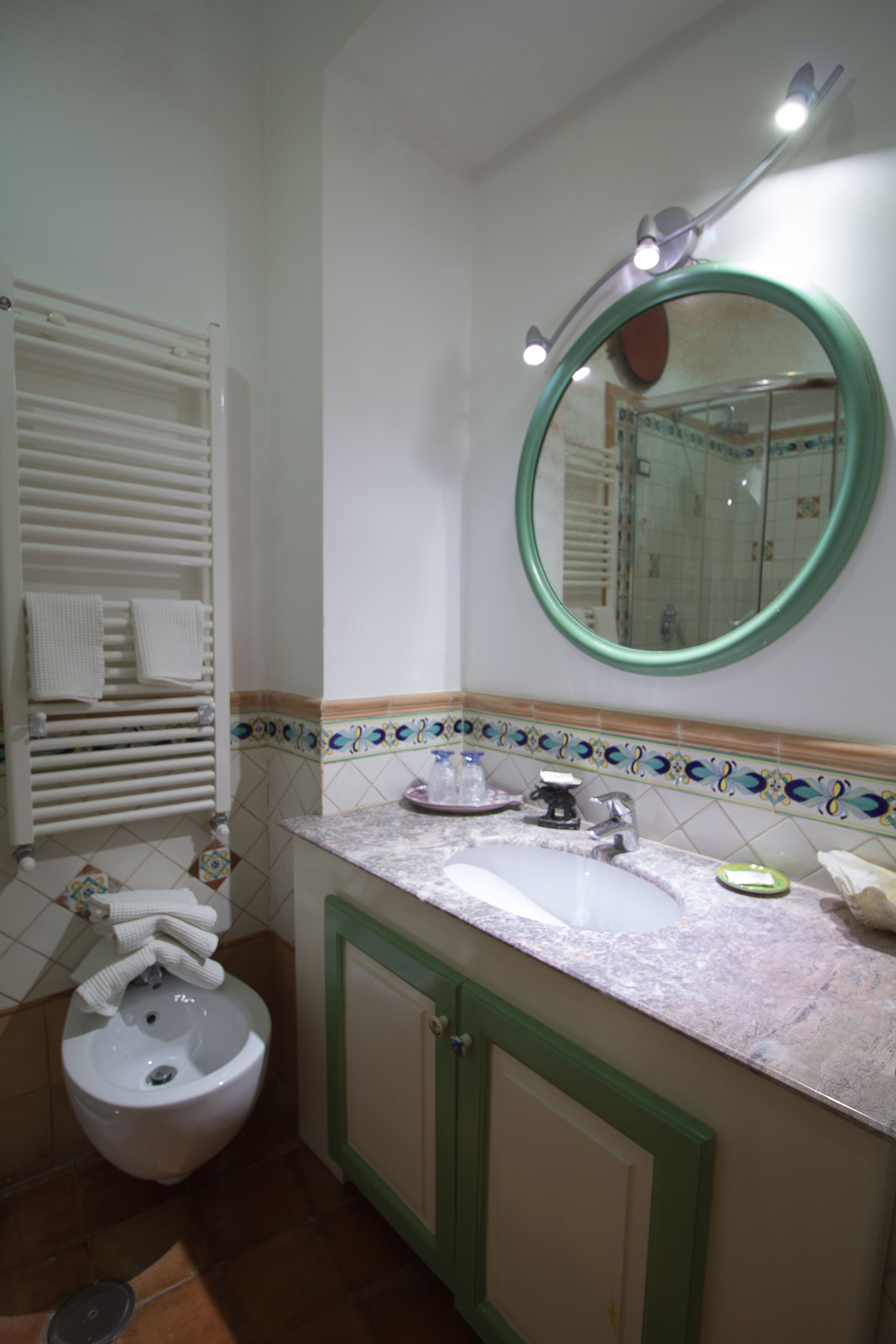 Une salle de bain avec un lavabo blanc, des meubles verts, des toilettes blanches et un miroir avec éclairage.