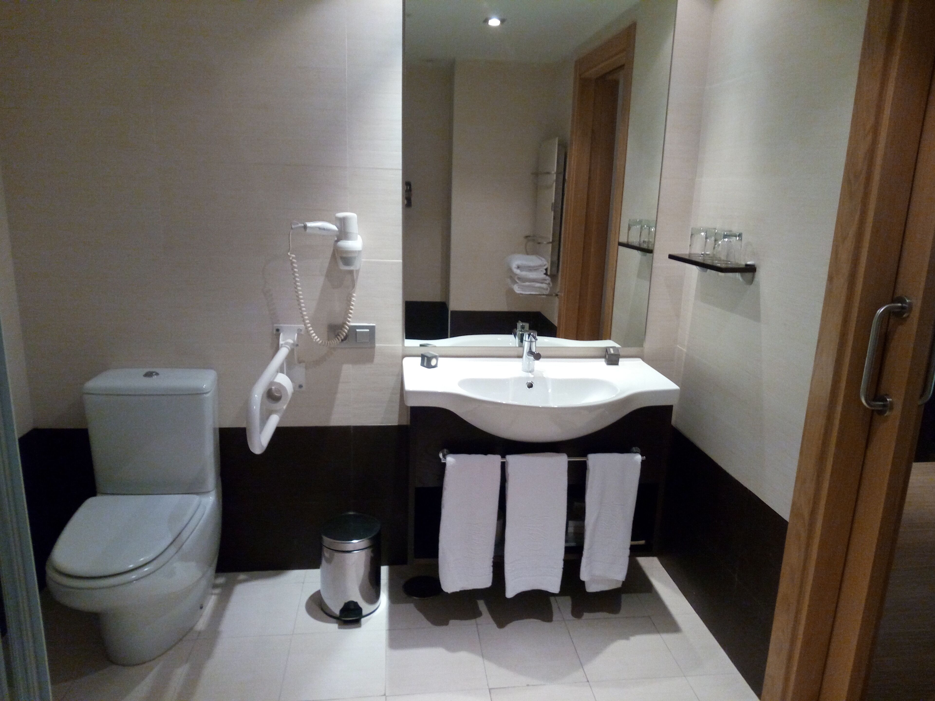 A modern bathroom with a toilet, bidet, sink, and a trash bin.
