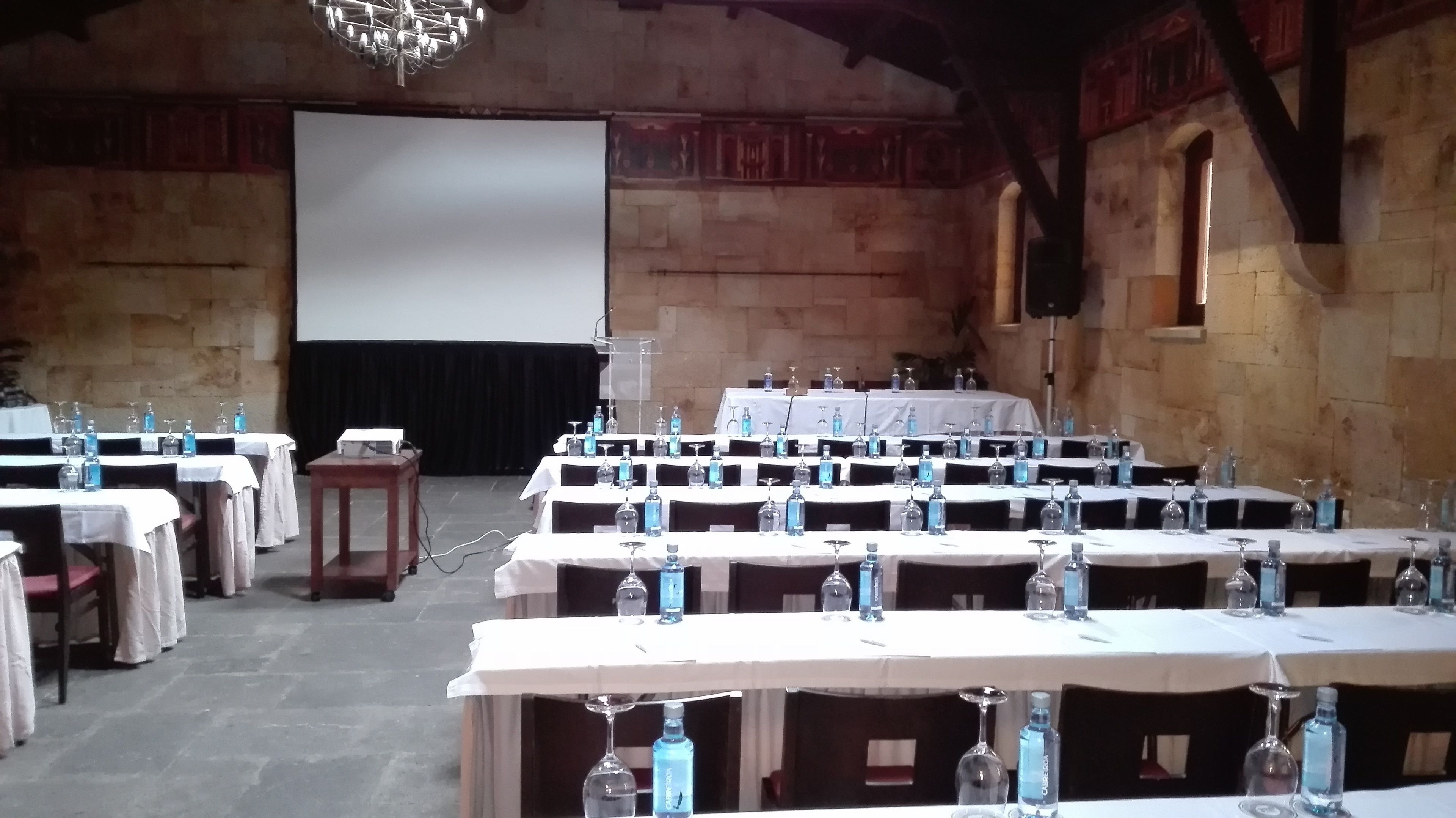 Une salle de conférence avec plusieurs tables disposées pour une réunion, chacune étant équipée de bouteilles d’eau et de verres.