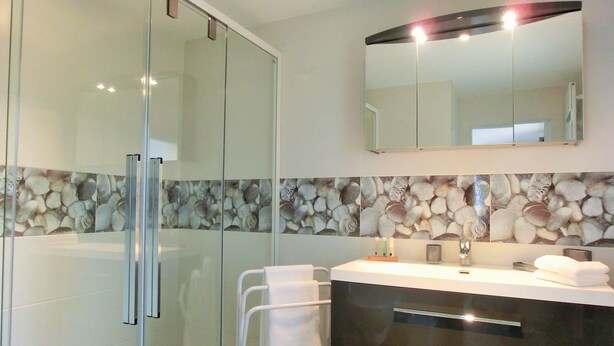 Un baño moderno con cabina de ducha de vidrio, tocador con espejo y salpicadero con diseño de piedra.