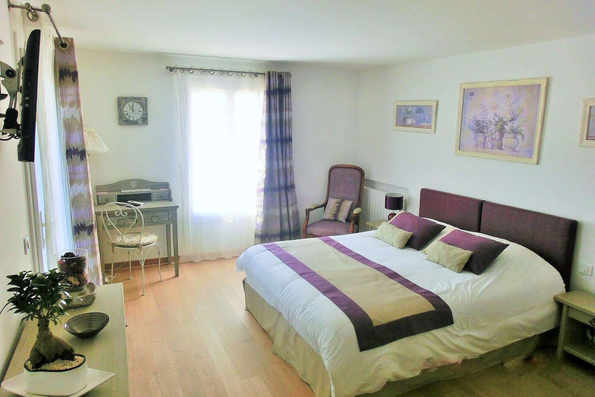 A bedroom with a bed, a desk, a chair, a potted plant, and two framed pictures on the wall.