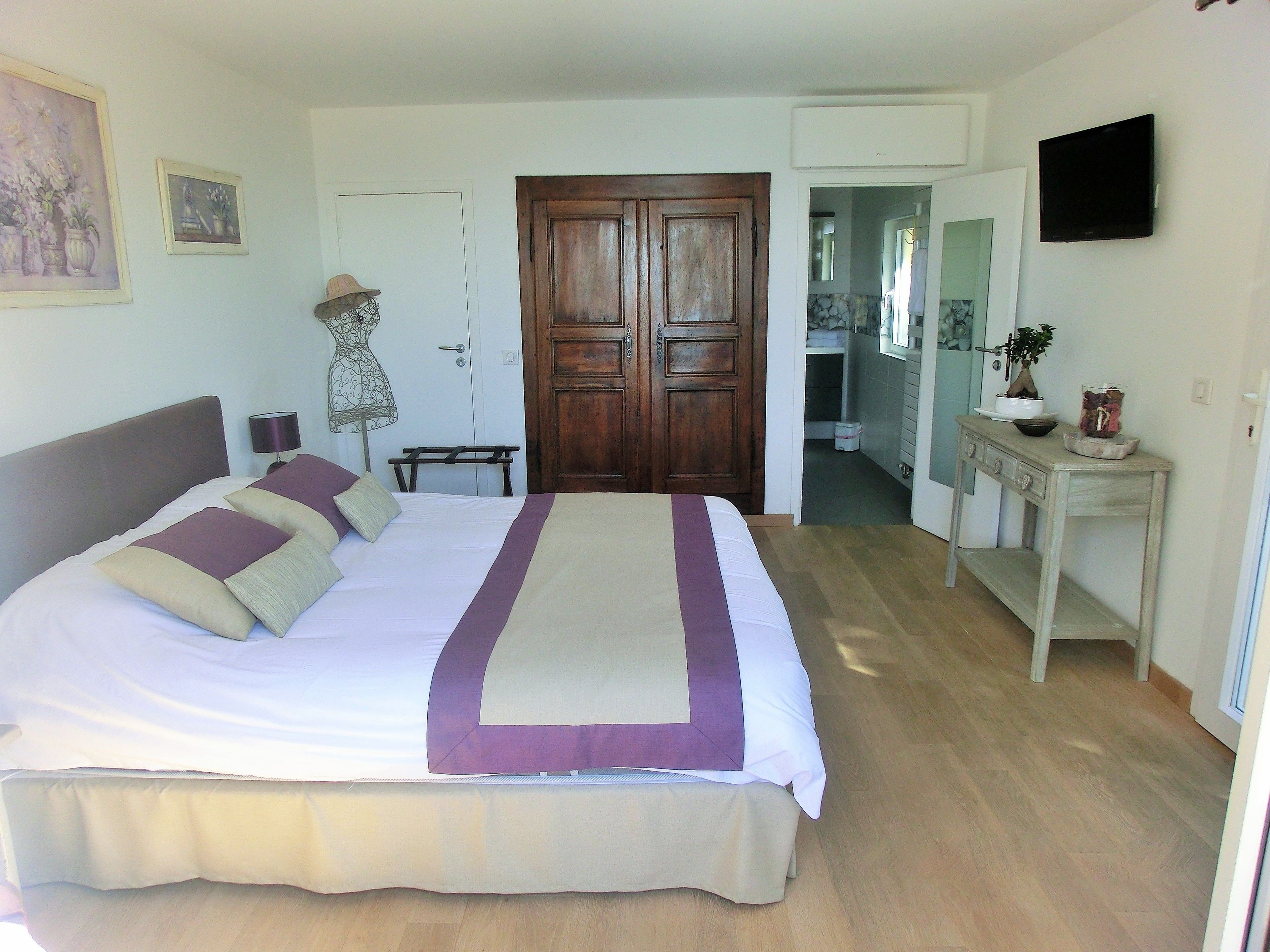 A neatly arranged bedroom with a large bed, a wooden door, a small table, and a television on the wall.