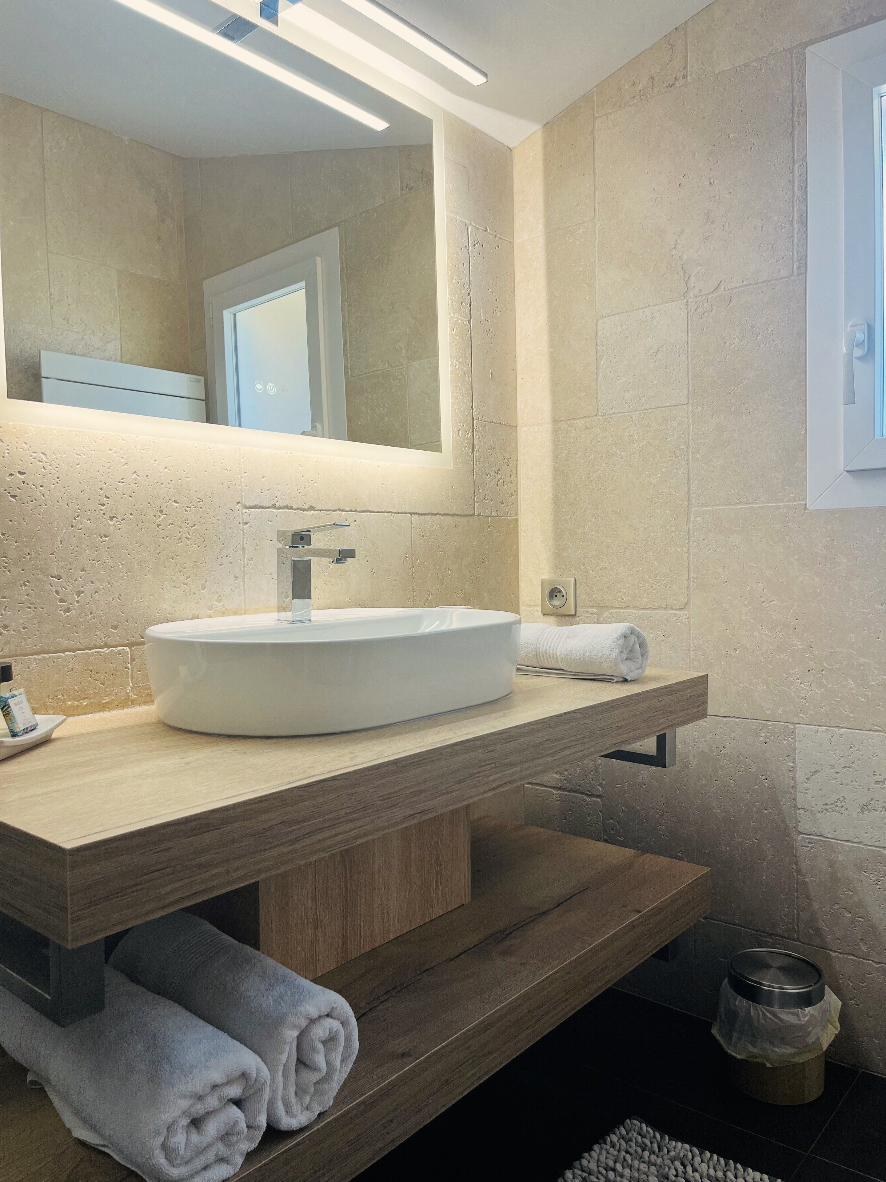 Une salle de bain moderne avec un grand miroir, un lavabo blanc et un meuble-lavabo en bois.