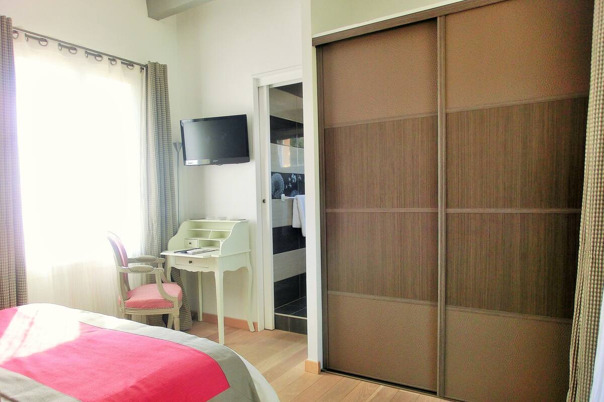 A bedroom with a bed, a desk, a chair, a television, and a sliding door.