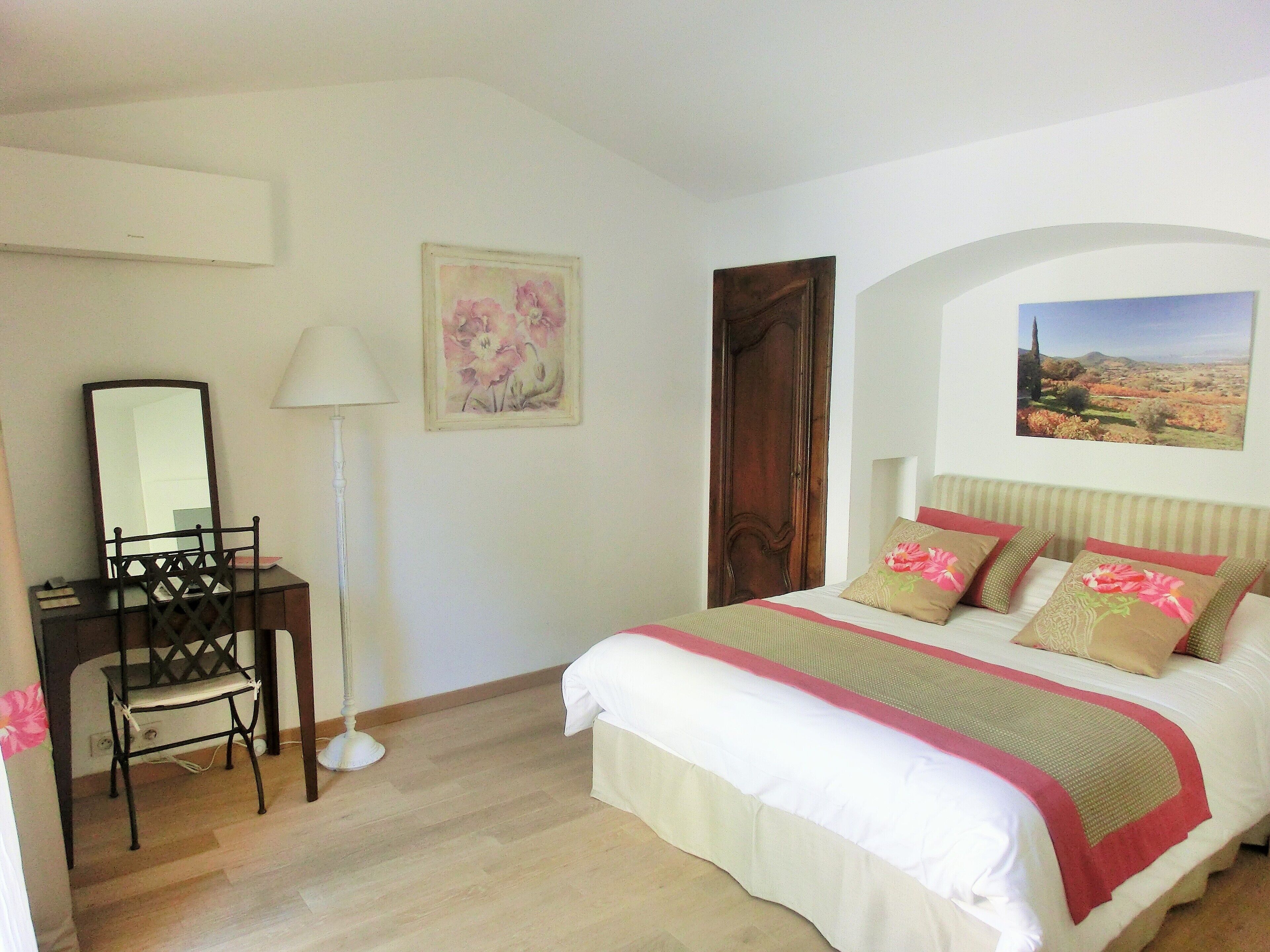 A bedroom with a bed, a desk, a chair, a lamp, and a painting on the wall.