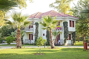 A two-story building with a red-tiled roof, surrounded by well-maintained lawns and palm trees. - Katrancı Park Hotel (Fethiye)